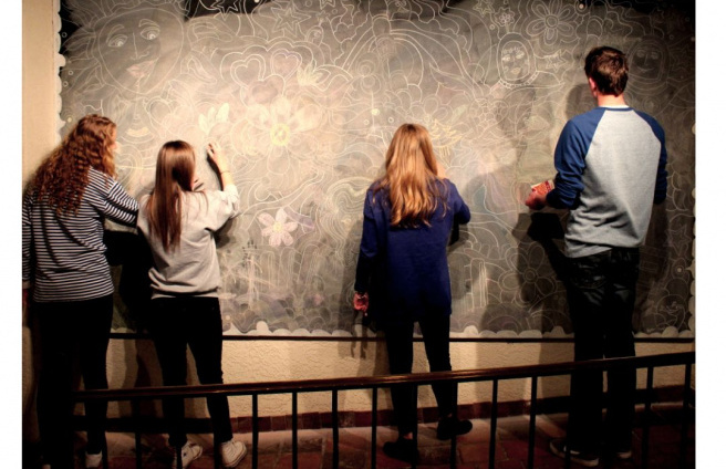 four teenagers drawing on a chalkboard wall