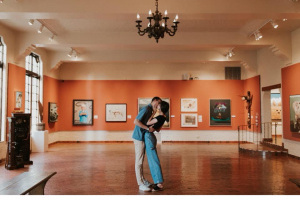 A man and woman kissing each other in a red-walled art gallery