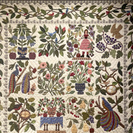 A quilt with a beige background and a floral leaf motif throughout